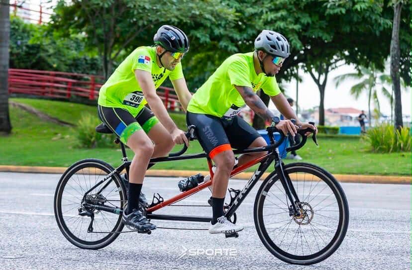 Dos ciclistas pedalean juntos en una bicicleta tándem por una carretera