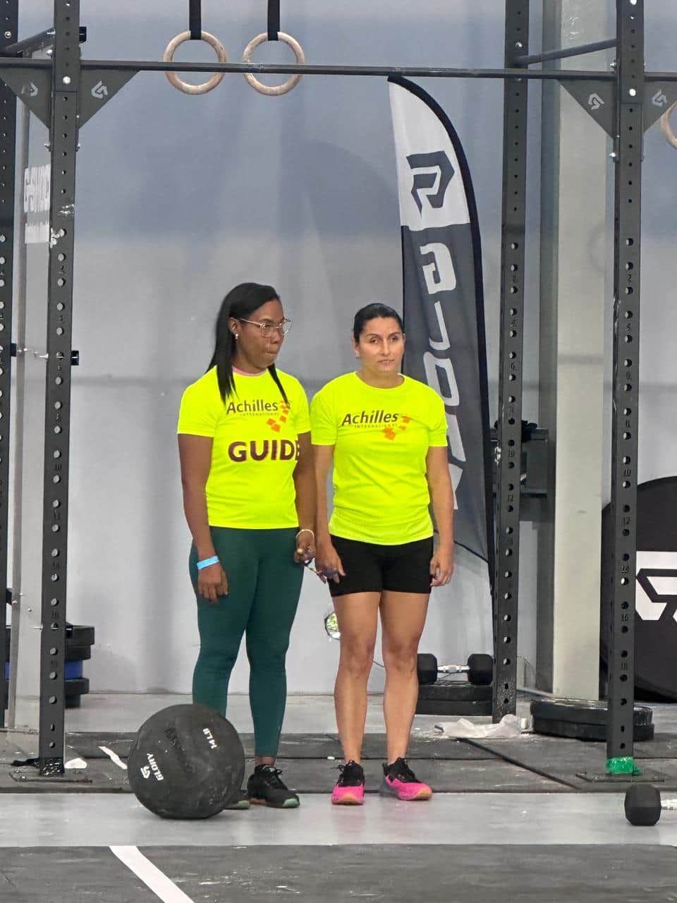 Una guía y una atleta, de pie, junto al material de entrenamiento del gimnasio