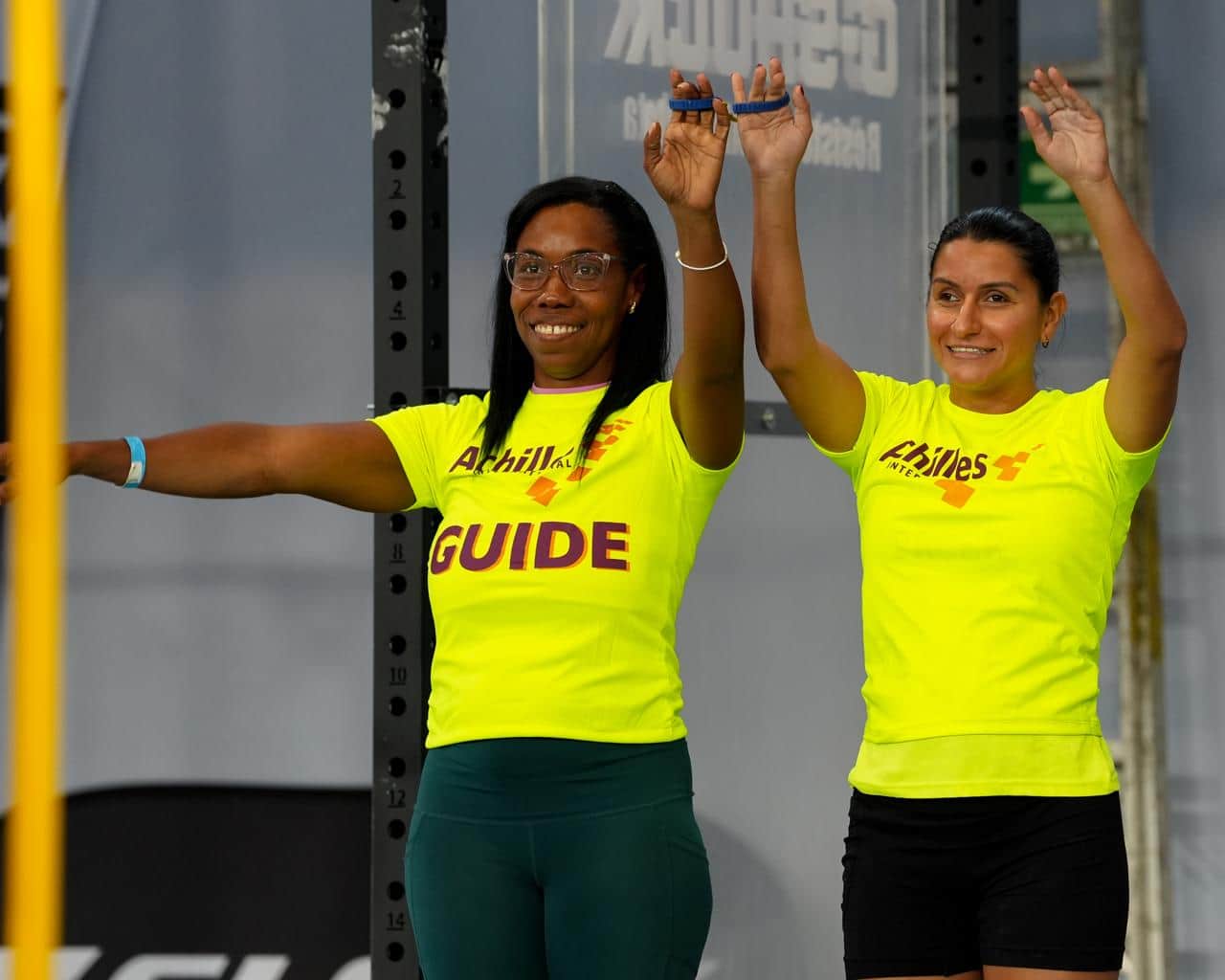 Una guía y una atleta levantan los brazos juntas dentro del gimnasio